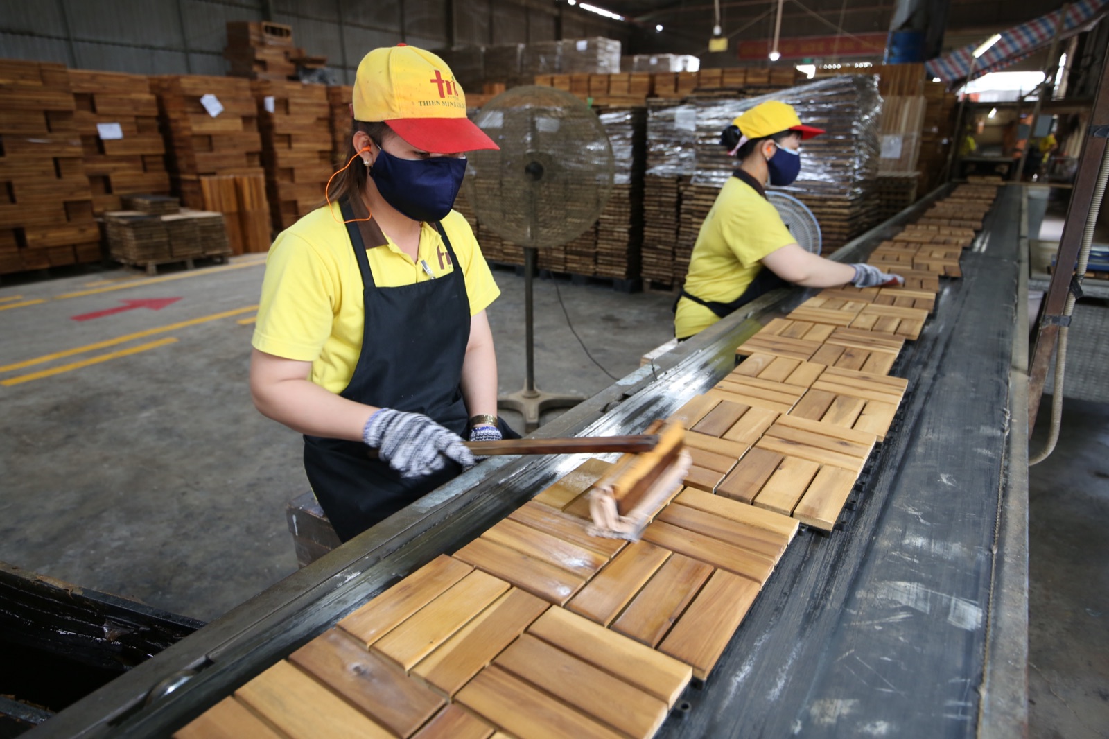 Workers applying protective oil finish to acacia tiles on the production line